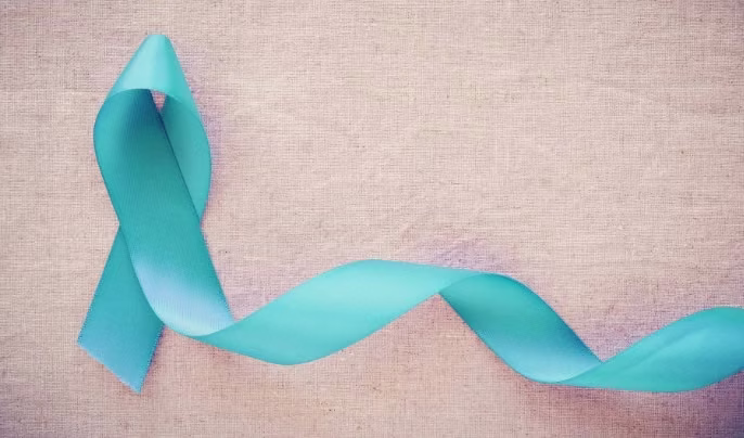 A teal awareness ribbon is shown against a beige textured background, symbolizing support often found at a medical center.