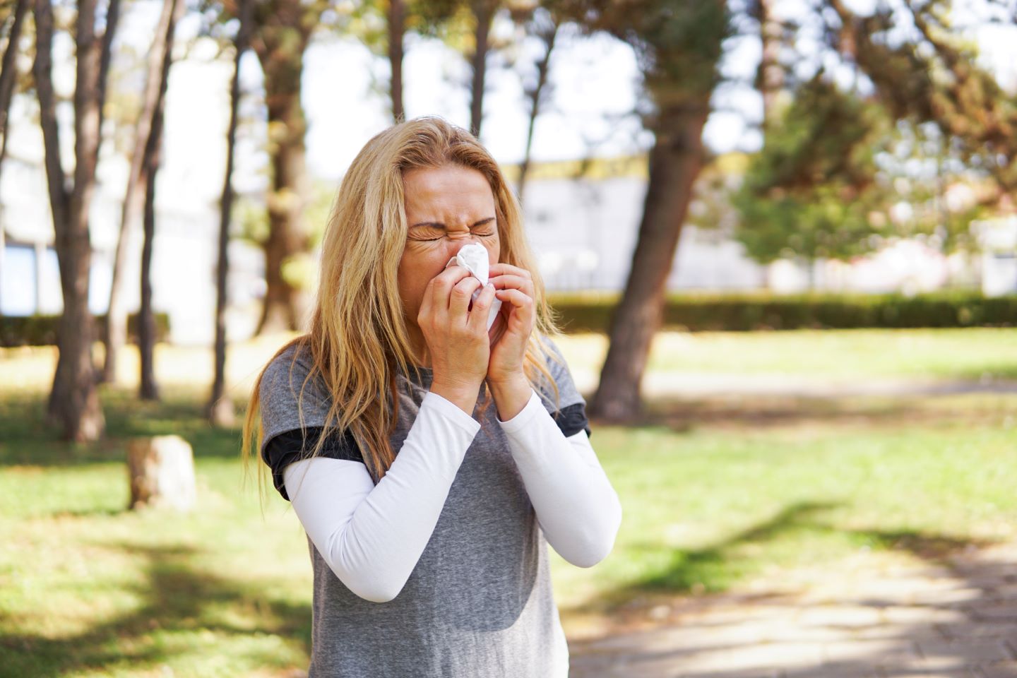 Woman suffering from spring allergy, blowing nose with a tissue in the parkWoman suffering from spring allergy, blowing nose with a tissue in the park