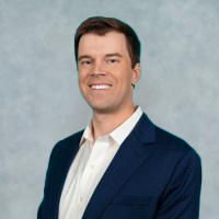 A man in a dark blue suit and white shirt smiling against a light, textured background, reminiscent of the professionalism you'd find at a top-tier medical center.