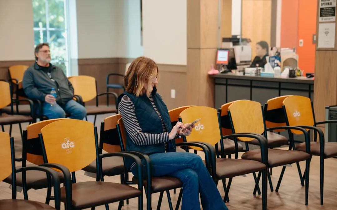 Woman waiting in an AFC Urgent Care lobby, typing on her phone.