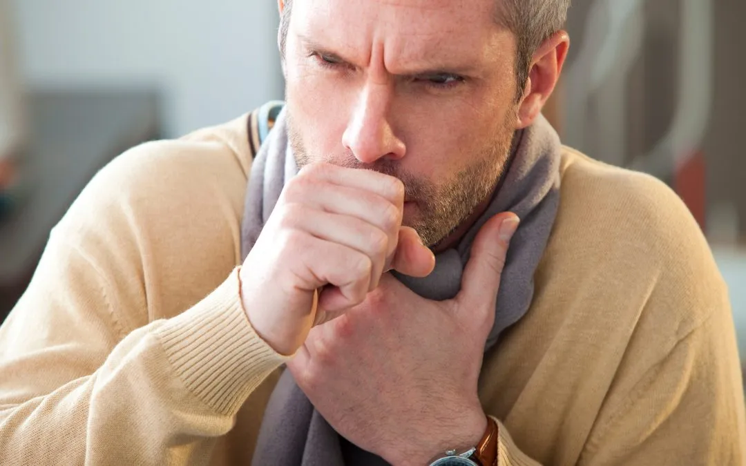 Man in tan sweater coughs into his hand